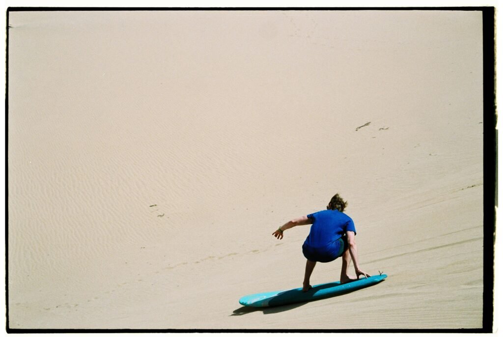 A thrilling sandboarding experience on the vast dunes of Morocco with a blue-sky backdrop.