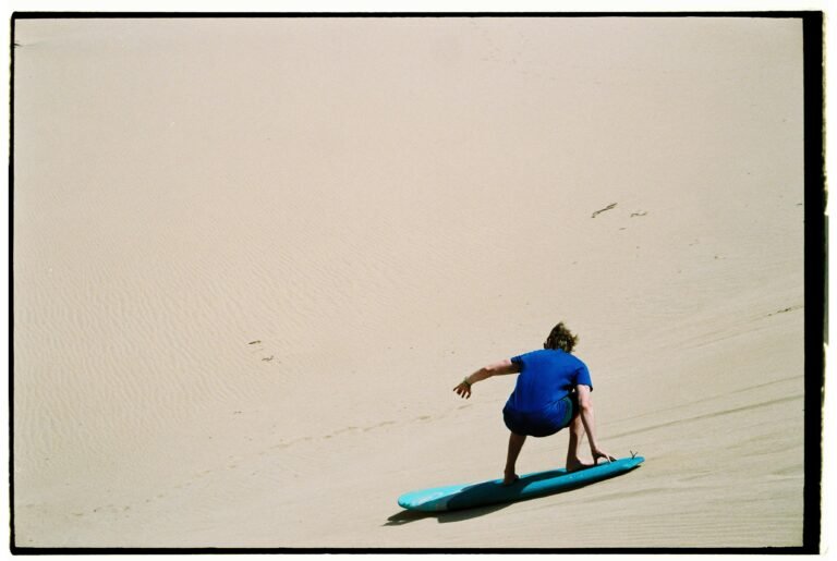 A thrilling sandboarding experience on the vast dunes of Morocco with a blue-sky backdrop.