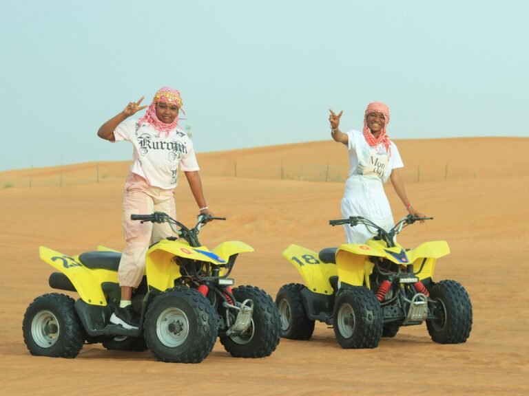 Two women enjoying a thrilling quad ride in the Dubai desert, posing energetically.