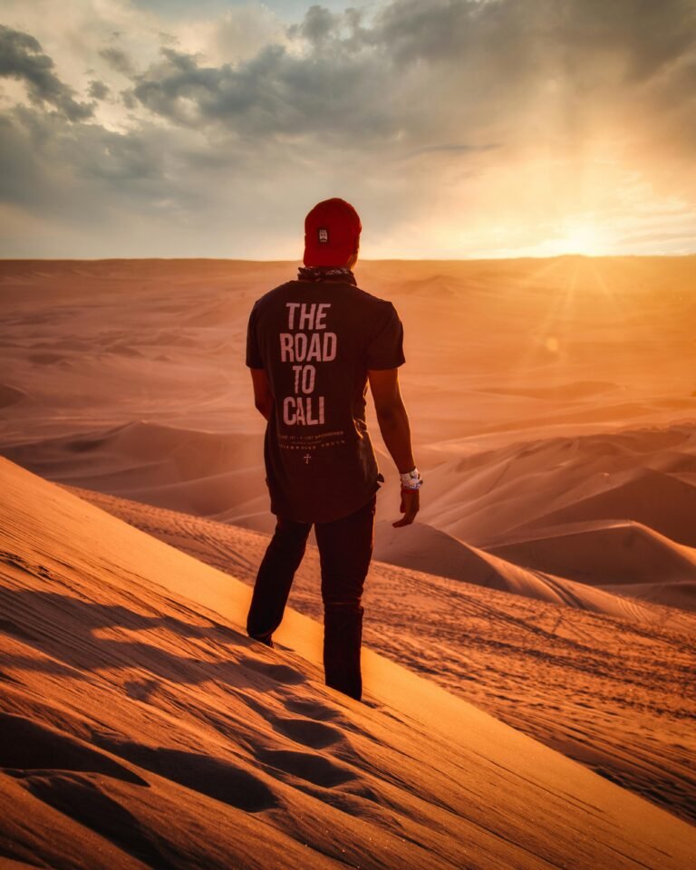 Man standing on sand dunes in Huacachina Desert, Peru at sunset, embracing solitude and adventure.