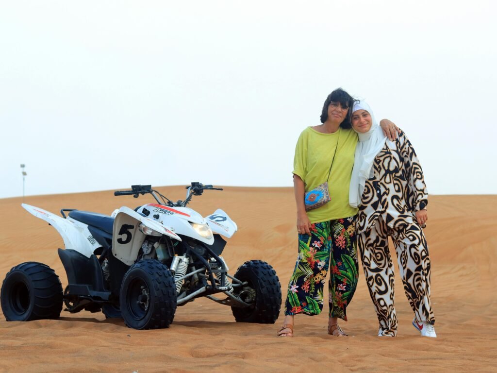 Two women stand with a quad bike in the Dubai desert, embracing adventure and friendship.