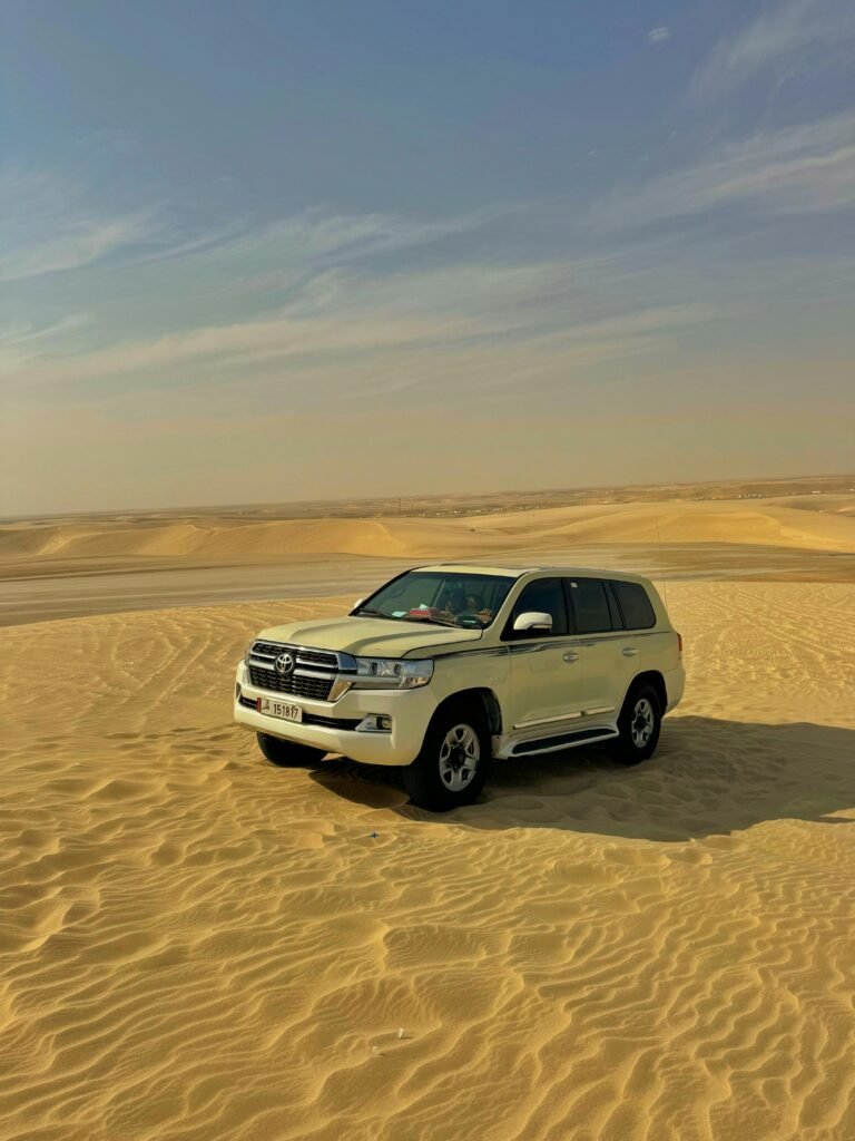 White SUV parked on the golden desert dunes under a clear sky in Qatar.